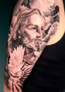 A black and grey realism style tattoo on a person's upper arm depicting the face of Jesus Christ with a white dove in the foreground