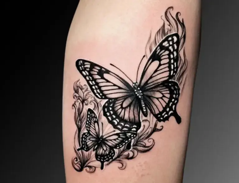 Black and gray tattoo of two detailed butterflies with intricate wing patterns, surrounded by flowing ornamental designs and swirling lines. The composition blends realism with decorative elements, giving the butterflies a dynamic and elegant appearance.