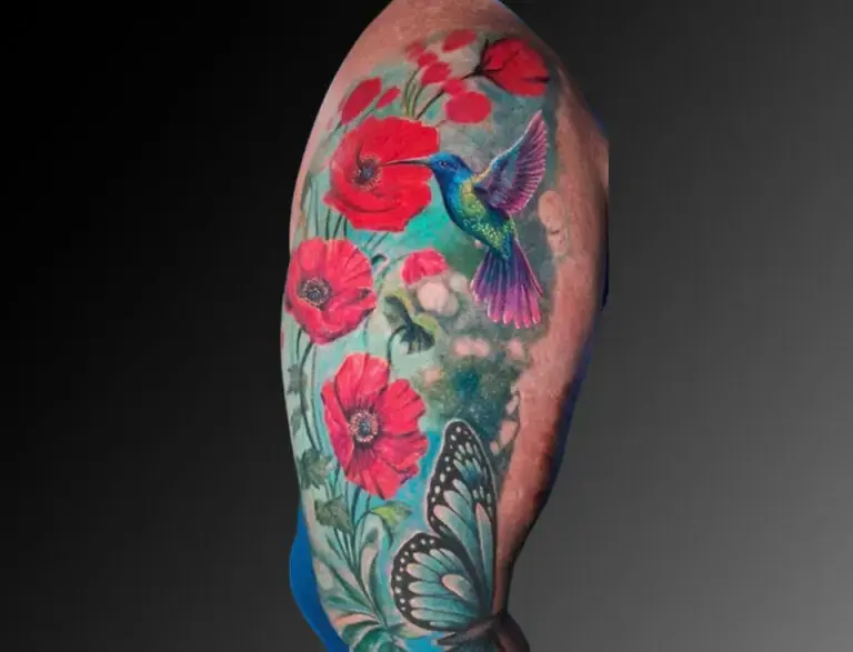 Colorful tattoo covering the upper arm, featuring vibrant red poppy flowers, a detailed hummingbird in flight with bright blue and purple hues, and a black and white butterfly near the bottom. The design is set against a soft green and blue background, creating a natural, garden-like scene.