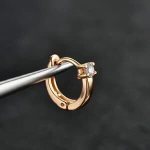 This image features a luxurious gold hoop earring adorned with a sparkling gemstone set in a sleek, polished design. This piece is ideal for a variety of piercings, such as: Helix Daith Septum Lobes The timeless elegance of gold combined with the brilliance of the stone makes it a perfect choice for clients looking for refined, statement jewelry.