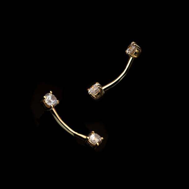 This image features a pair of gold curved barbell piercings with sparkling clear gemstones on both ends. Perfect for navel piercings or curated looks, their elegant simplicity combines timeless luxury with versatility.